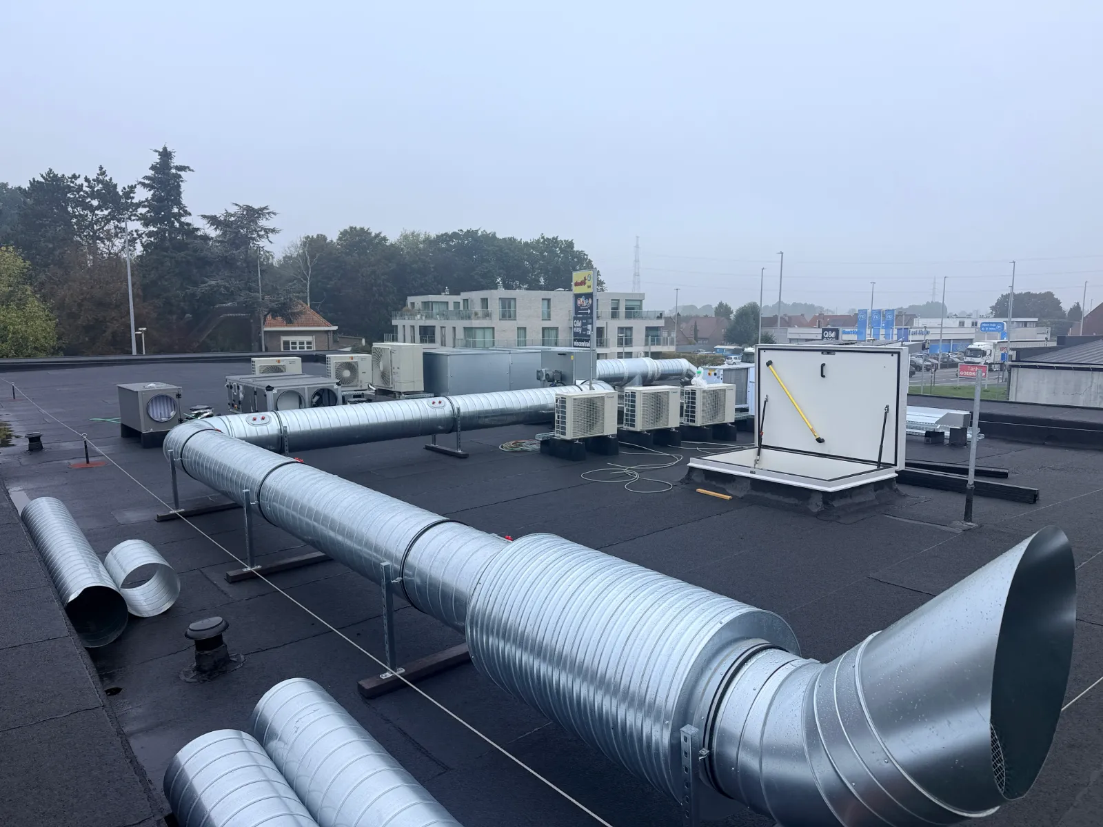 Technische installaties op het platte dak van een gebouw: ventilatieleidingen, buitenunits van warmtepompen en een dakluik